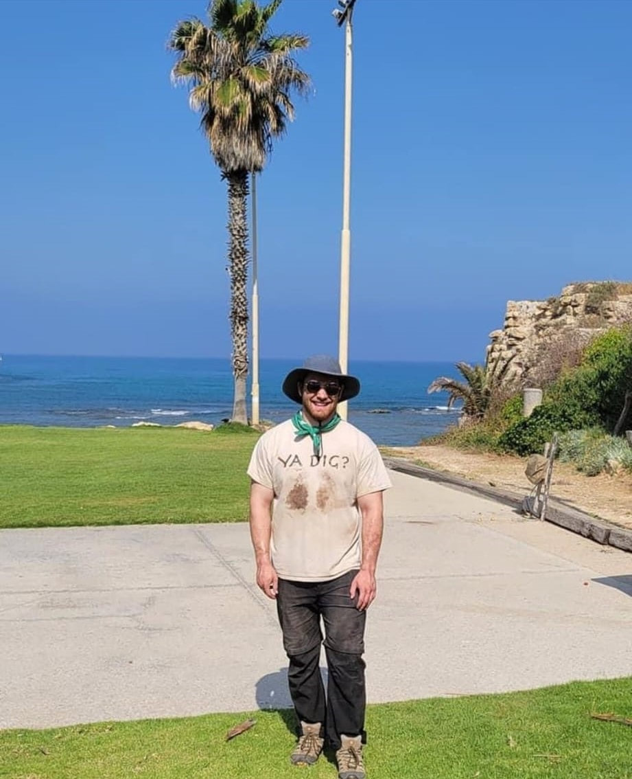Man with floppy hat and sunglasses standing in front of a palm tree on the beach