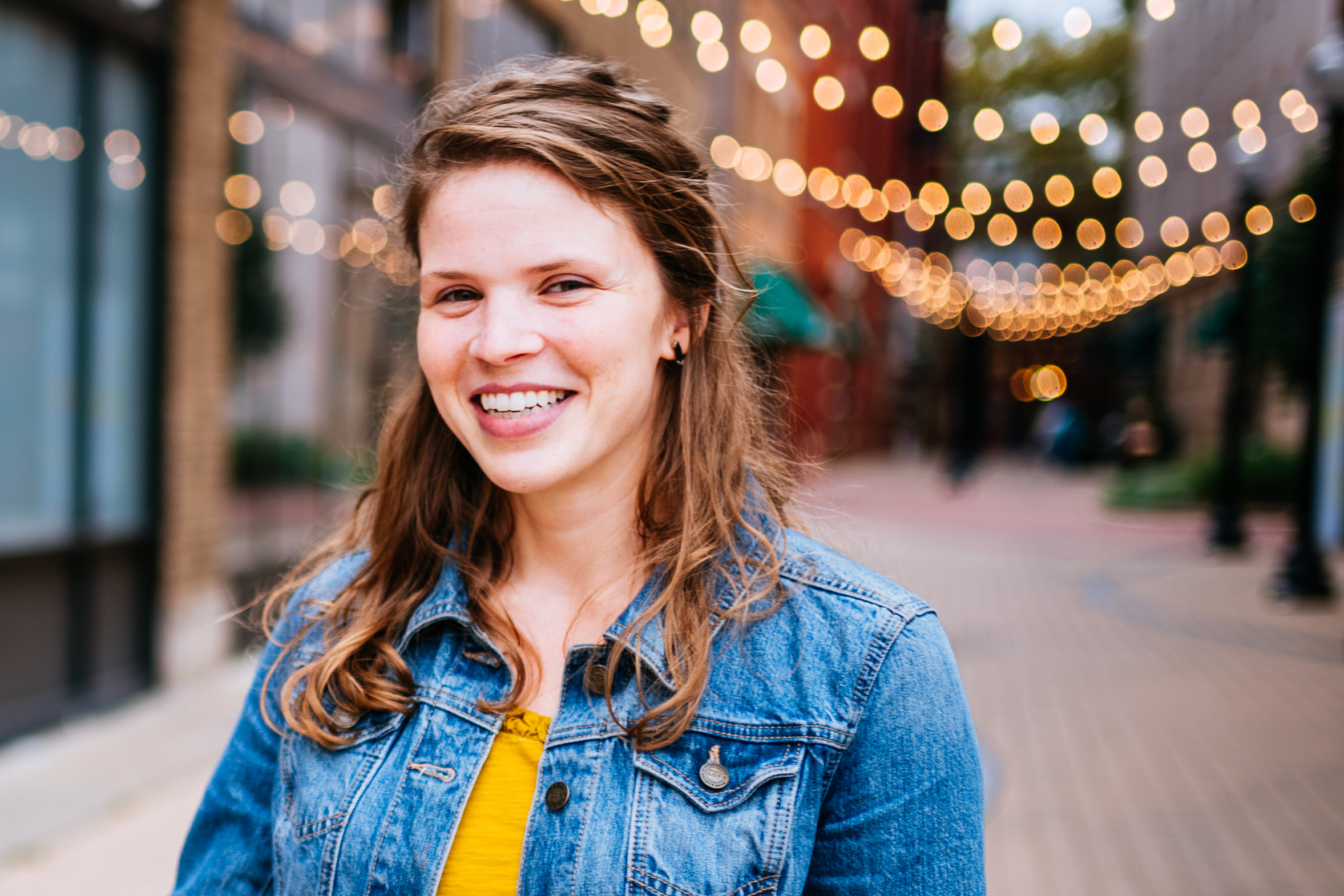 woman in a blue denim jacket and yellow shirt smiling at the viewer