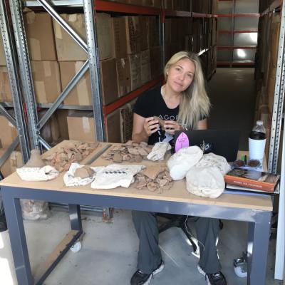 blond woman sitting at a table in a warehouse sorting artefacts