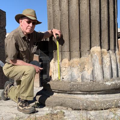 Man kneeling next to a column in the pompeii forum with a tape measure