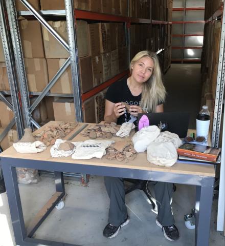 blond woman sitting at a table in a warehouse sorting artefacts