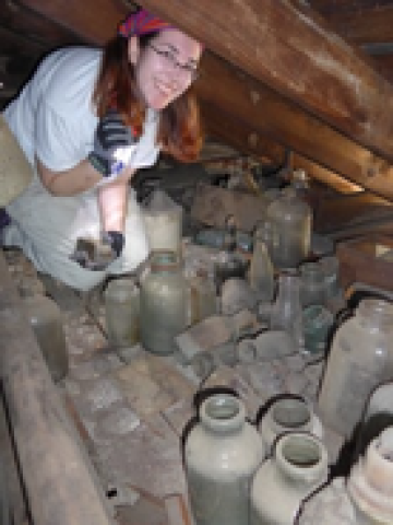 woman with a flashlight crouching in an attic full of glassware