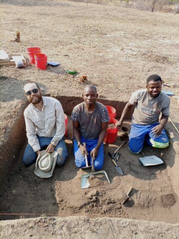 3 archaeologists in a trench looking at the viewer